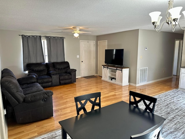 living room with baseboards, light wood-style flooring, visible vents, and a textured ceiling