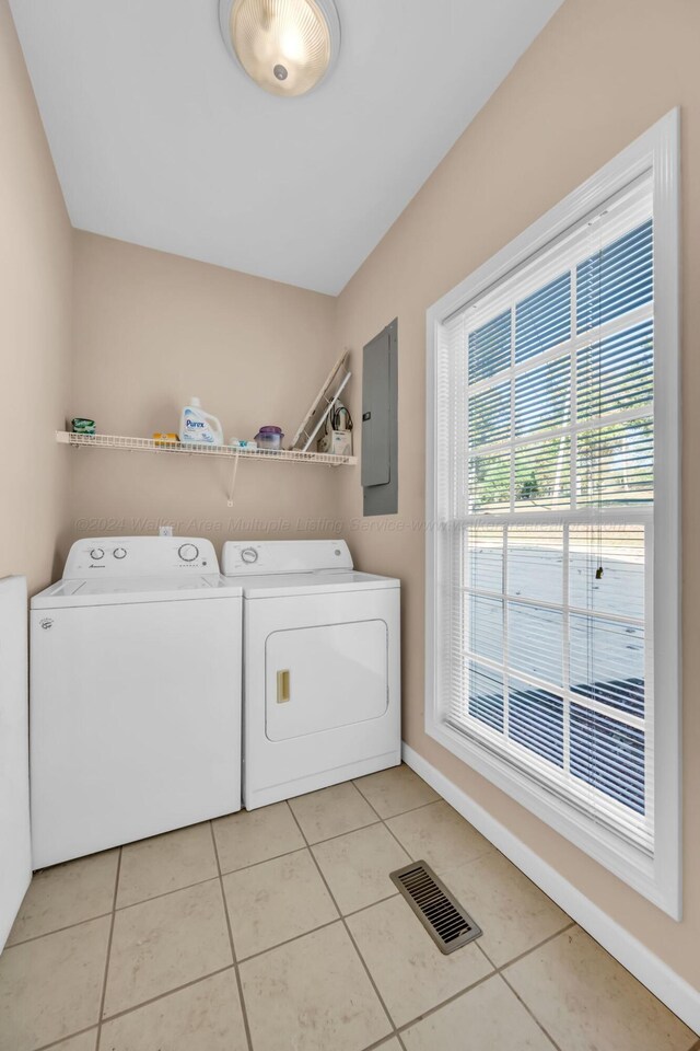 clothes washing area featuring electric panel, light tile patterned floors, and washer and dryer