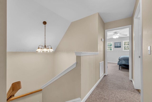 hall featuring light colored carpet, lofted ceiling, and a notable chandelier