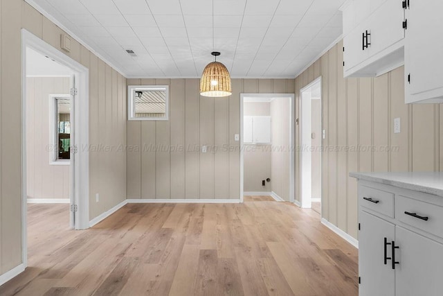 unfurnished dining area with crown molding, wooden walls, and light wood-type flooring