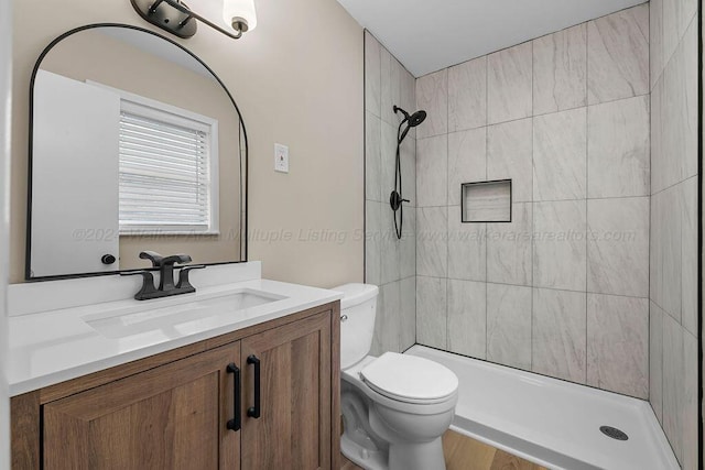 bathroom with hardwood / wood-style floors, vanity, toilet, and tiled shower