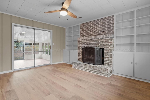 unfurnished living room featuring crown molding, a brick fireplace, ceiling fan, built in features, and light hardwood / wood-style floors