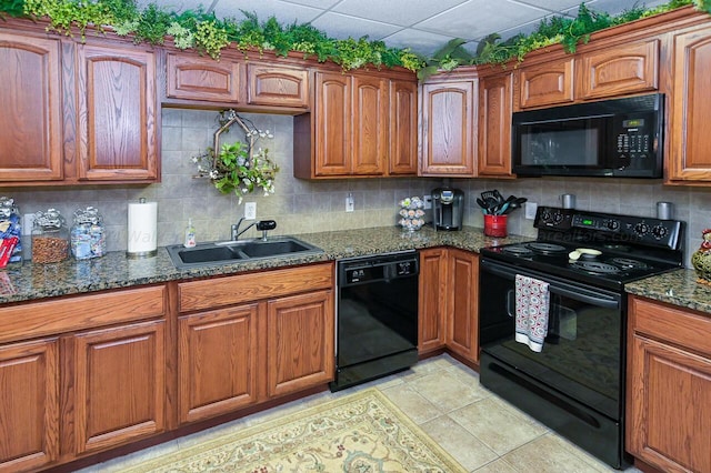 kitchen featuring brown cabinets, black appliances, a sink, dark stone countertops, and backsplash