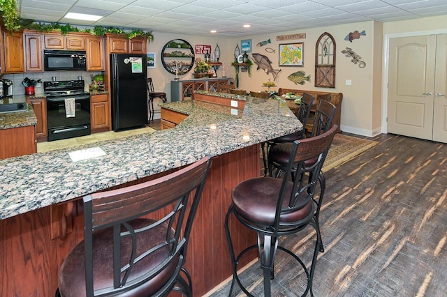 kitchen featuring brown cabinets, wood finished floors, black appliances, a paneled ceiling, and a sink