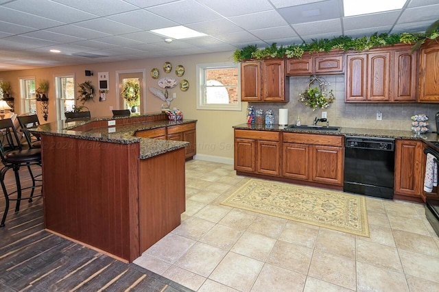 kitchen with a breakfast bar, dark stone counters, a sink, decorative backsplash, and black dishwasher