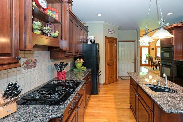 kitchen with light wood finished floors, dark stone counters, ornamental molding, a sink, and black appliances