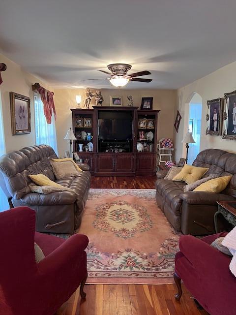 living area with arched walkways, a ceiling fan, and wood finished floors