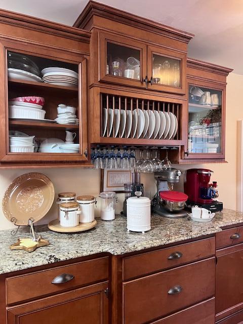 interior space featuring glass insert cabinets, light stone countertops, and brown cabinetry