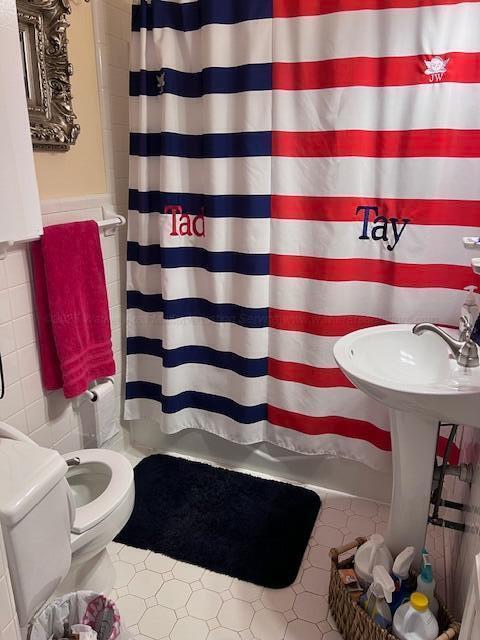 bathroom featuring curtained shower, toilet, tile walls, and wainscoting