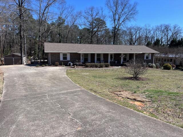 ranch-style home featuring an outbuilding, a front lawn, covered porch, and driveway