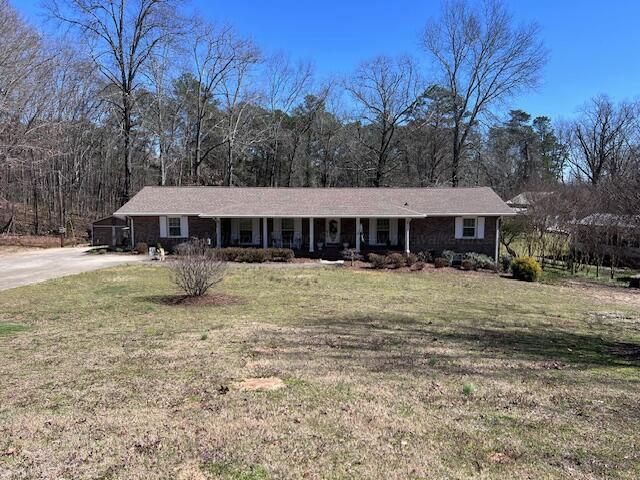 ranch-style home with dirt driveway, a porch, and a front lawn