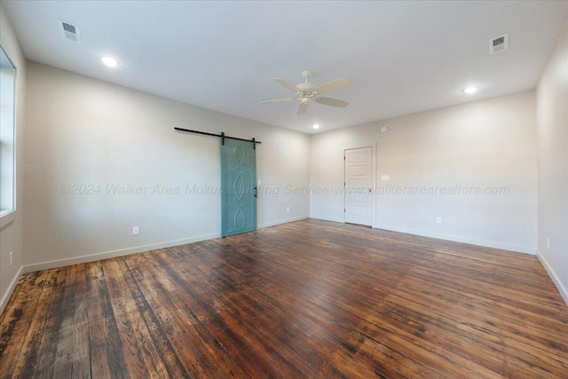 empty room with ceiling fan, a barn door, and dark hardwood / wood-style flooring