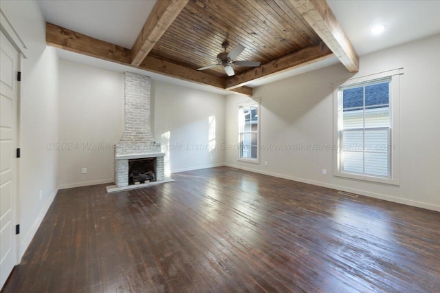 unfurnished living room featuring beamed ceiling, dark hardwood / wood-style flooring, a brick fireplace, and ceiling fan