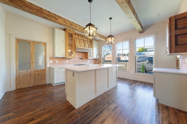 kitchen featuring dark hardwood / wood-style flooring, tasteful backsplash, a kitchen island with sink, decorative light fixtures, and white cabinets