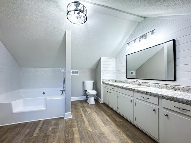 bathroom with hardwood / wood-style flooring, a textured ceiling, vaulted ceiling, a bathing tub, and vanity