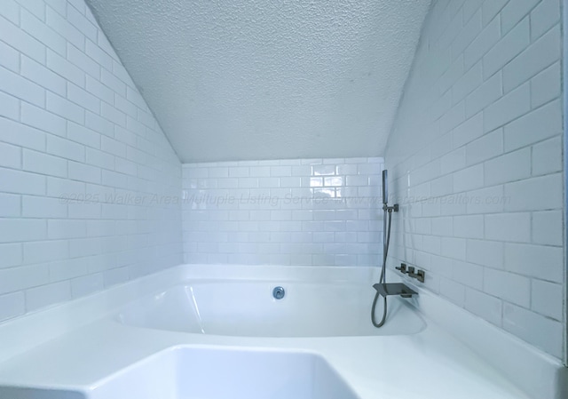 bathroom with lofted ceiling, a tub to relax in, and a textured ceiling