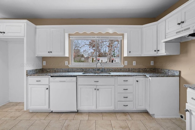 kitchen featuring white dishwasher, sink, light tile patterned floors, dark stone countertops, and white cabinetry