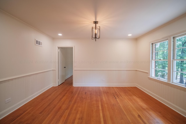 empty room with crown molding, light hardwood / wood-style floors, and a notable chandelier