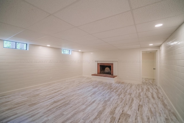 basement with plenty of natural light, a drop ceiling, light wood-type flooring, and a brick fireplace