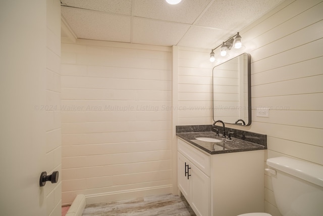 bathroom with vanity, hardwood / wood-style floors, a paneled ceiling, and wooden walls