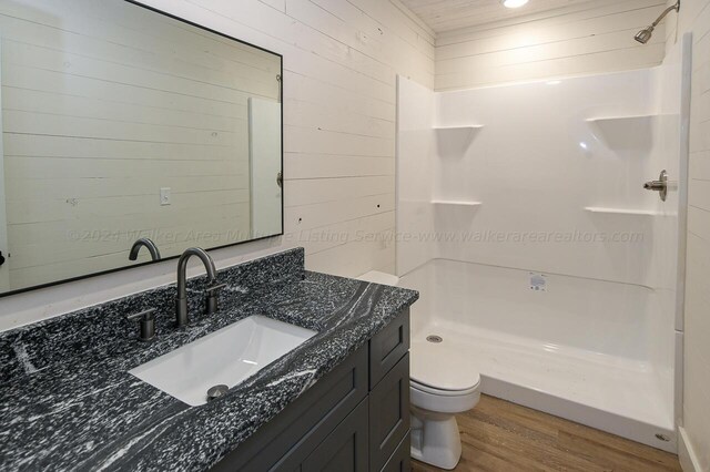 bathroom with toilet, vanity, wood walls, wood-type flooring, and a shower