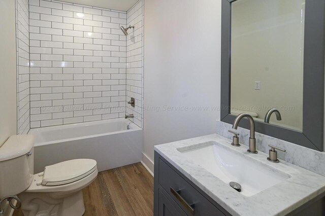 full bathroom with toilet, tiled shower / bath, vanity, and hardwood / wood-style floors