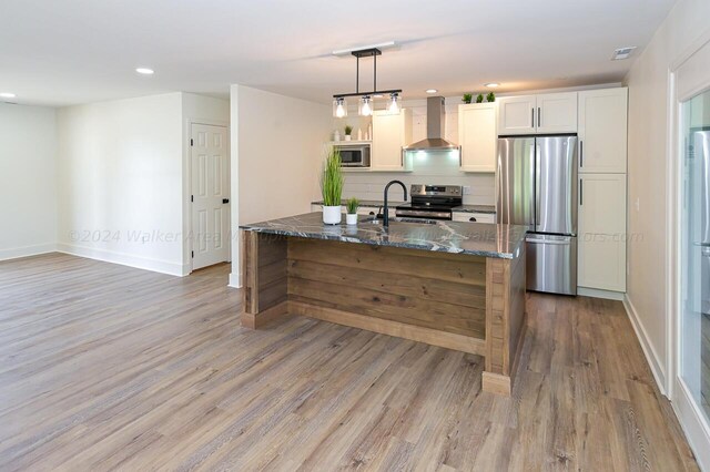 kitchen featuring decorative light fixtures, dark stone counters, white cabinetry, stainless steel appliances, and wall chimney exhaust hood