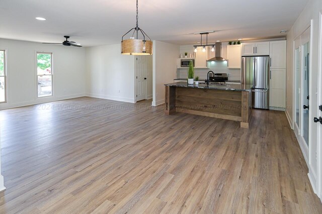 kitchen with appliances with stainless steel finishes, white cabinetry, hanging light fixtures, and wall chimney range hood