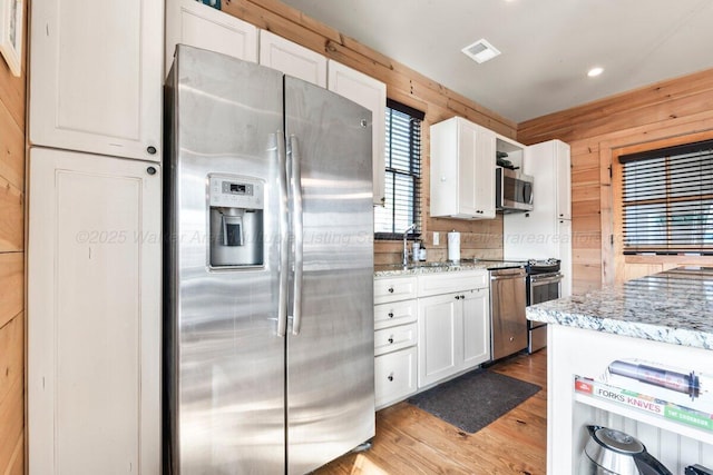 kitchen featuring stainless steel appliances, wooden walls, white cabinets, and light stone countertops