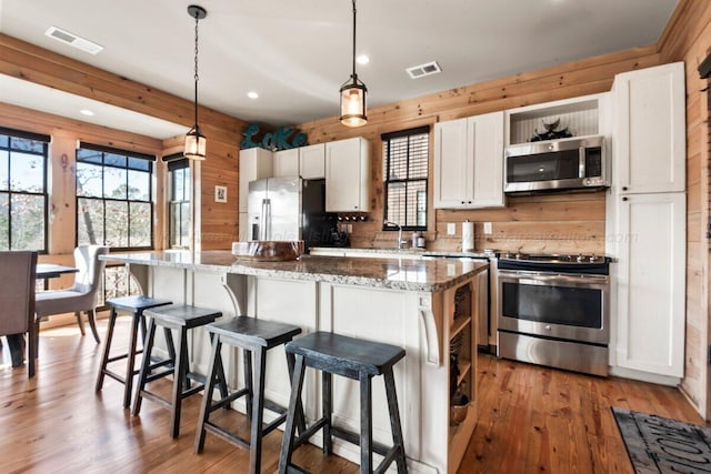 kitchen featuring a center island, decorative light fixtures, stainless steel appliances, stone countertops, and white cabinets