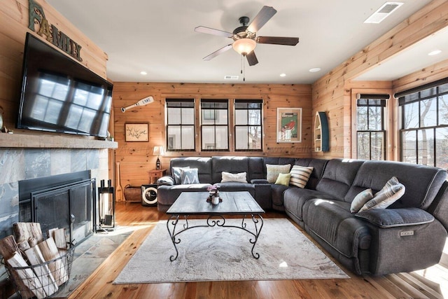 living room featuring a tiled fireplace, wood walls, ceiling fan, and light hardwood / wood-style flooring