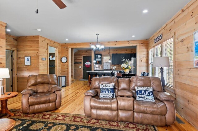 living room with ceiling fan with notable chandelier, light hardwood / wood-style floors, and wooden walls