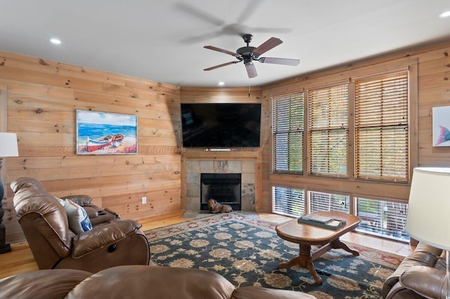 living room with a tiled fireplace, wooden walls, ceiling fan, and hardwood / wood-style flooring