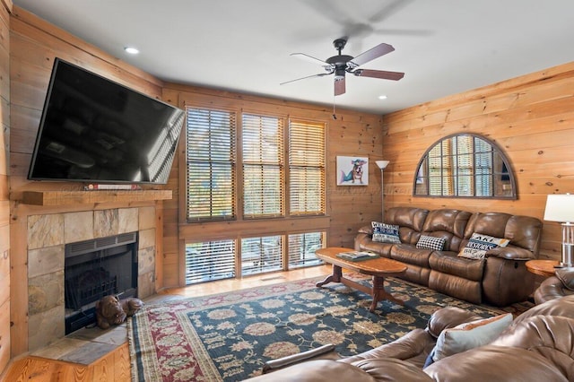 living room with ceiling fan, light wood-type flooring, wooden walls, and a tiled fireplace