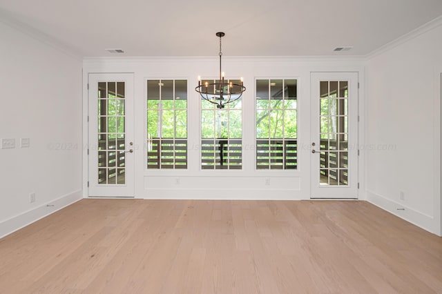 empty room with light hardwood / wood-style floors, an inviting chandelier, plenty of natural light, and crown molding