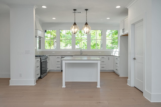 kitchen featuring a center island, white cabinets, crown molding, stainless steel gas stove, and light wood-type flooring