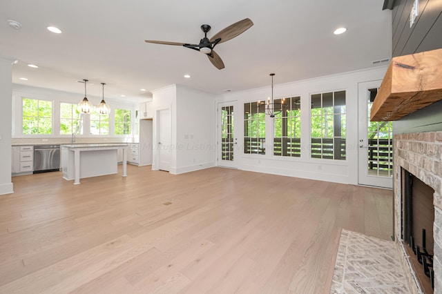 unfurnished living room featuring ornamental molding, ceiling fan with notable chandelier, sink, a fireplace, and light hardwood / wood-style floors