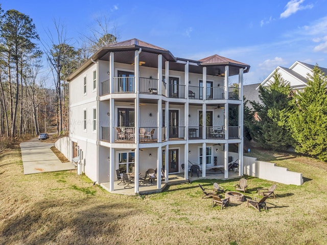 back of house with a lawn, ceiling fan, an outdoor fire pit, a patio area, and a balcony