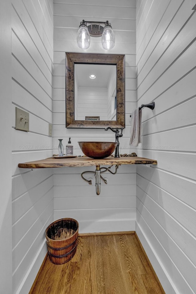 bathroom featuring hardwood / wood-style floors, wooden walls, and sink