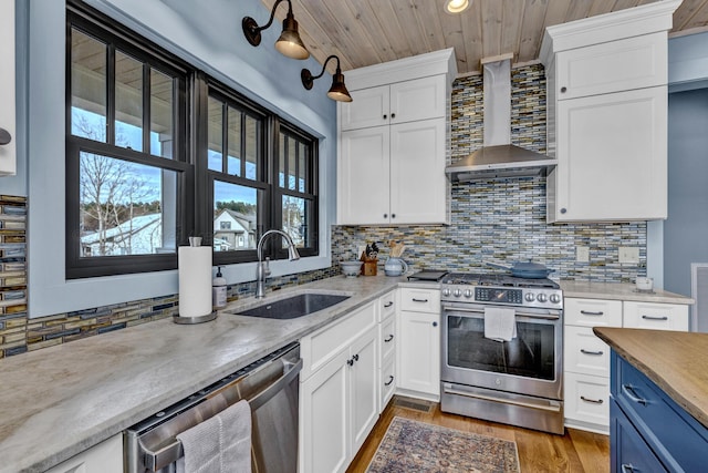 kitchen with sink, wall chimney exhaust hood, decorative backsplash, white cabinets, and appliances with stainless steel finishes