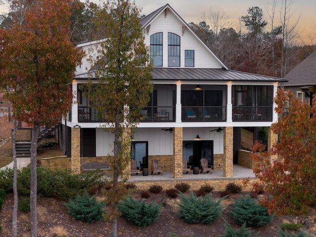 back house at dusk with a fireplace, a balcony, and a patio