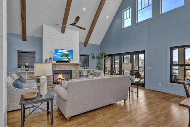 living room featuring beam ceiling, ceiling fan, high vaulted ceiling, a fireplace, and light wood-type flooring