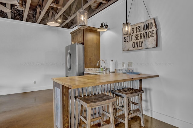 kitchen with stainless steel refrigerator, sink, hanging light fixtures, a kitchen breakfast bar, and butcher block countertops