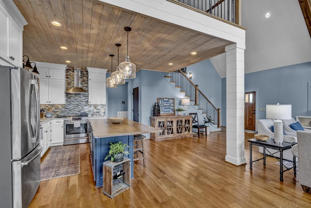 kitchen with wall chimney exhaust hood, stainless steel appliances, white cabinets, a center island, and hanging light fixtures