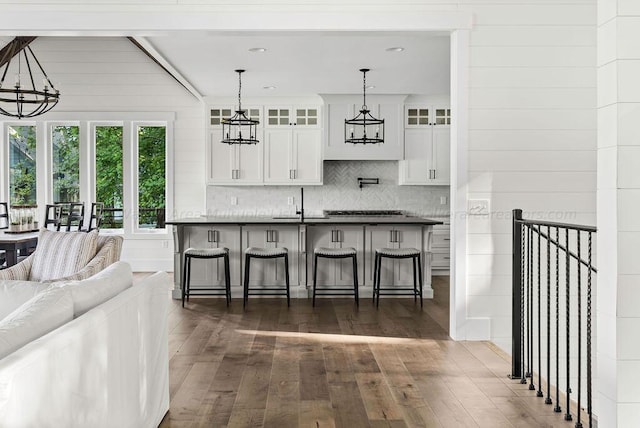 kitchen featuring wood walls, dark wood-type flooring, a kitchen breakfast bar, decorative light fixtures, and white cabinetry