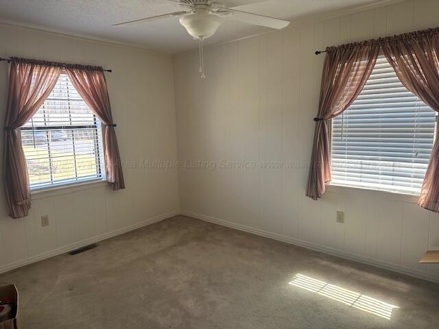 carpeted empty room with visible vents, baseboards, and a ceiling fan