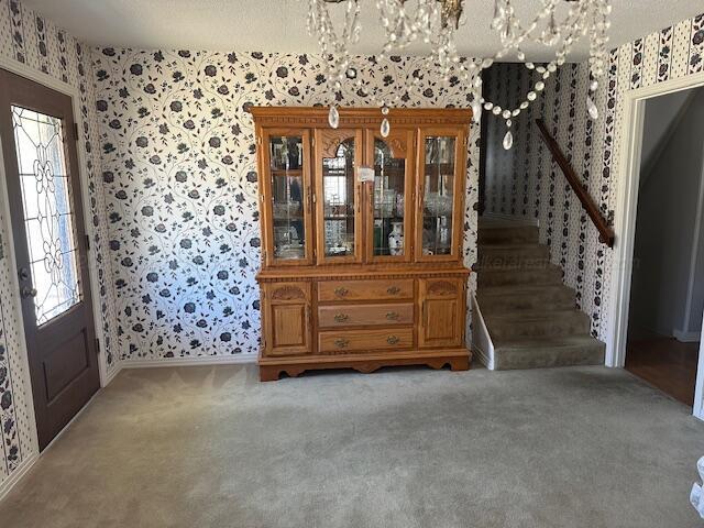 carpeted entrance foyer featuring baseboards, a notable chandelier, stairs, and wallpapered walls