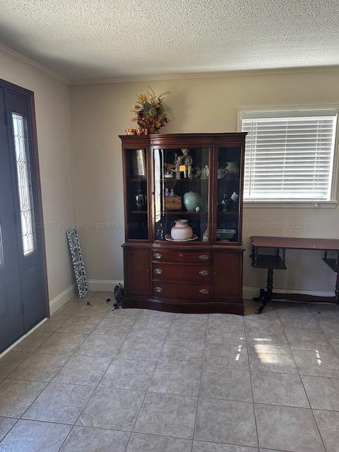 entryway featuring light tile patterned floors, baseboards, a textured ceiling, and ornamental molding