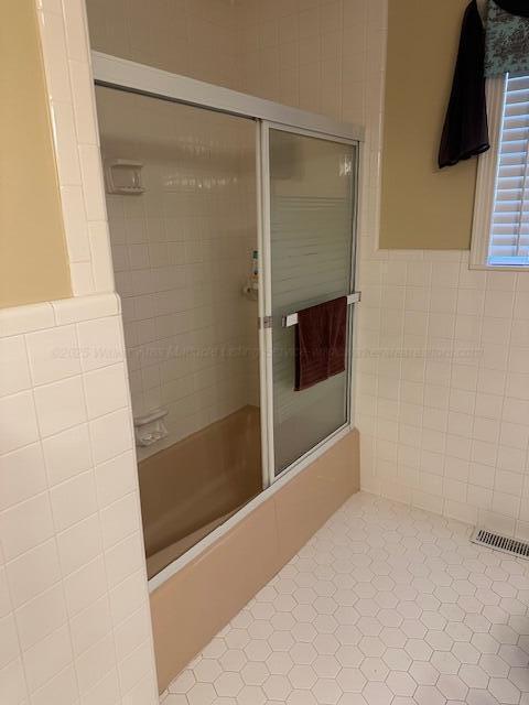 bathroom featuring a wainscoted wall, visible vents, tile patterned flooring, tile walls, and combined bath / shower with glass door