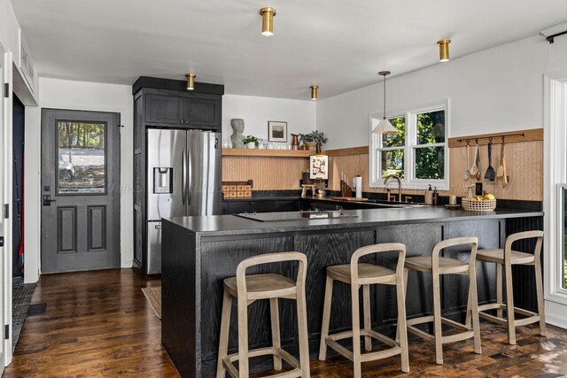 kitchen with black electric stovetop, dark hardwood / wood-style floors, kitchen peninsula, stainless steel fridge, and a breakfast bar